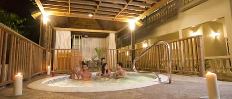 A hot tub area with wooden railings, a ceiling with wooden beams, and candles on the floor.