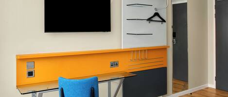 Una habitación moderna con cama, escritorio con silla, televisor montado en la pared y armario con espejo.