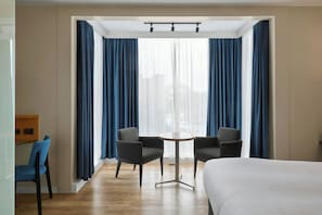 A hotel room with a bed, two armchairs, a small table, and a window with blue curtains. - Four Points Flex by Sheraton Newcastle (Newcastle-upon-Tyne)