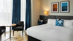 A hotel room with a bed, a chair, a small table, a lamp, and two framed pictures on the wall. - Four Points Flex by Sheraton Newcastle (Newcastle-upon-Tyne)