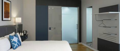 A modern hotel room with a large bed, bedside table, lamp, and a wardrobe with a mirror.