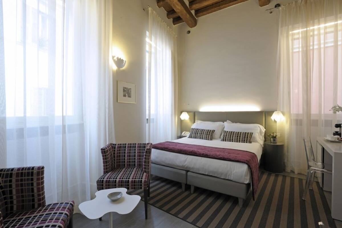 Una camera d'albergo con un letto, due sedie, un tavolino e una scrivania con una lampada.