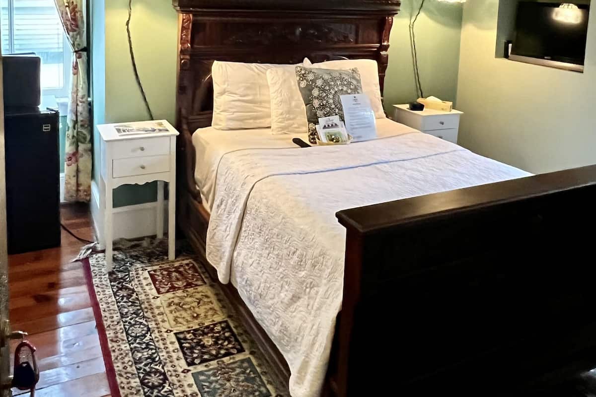 Una camera da letto con un letto di legno, una ventola a soffitto, lampade ai comodini, un televisore e un tappeto decorato.