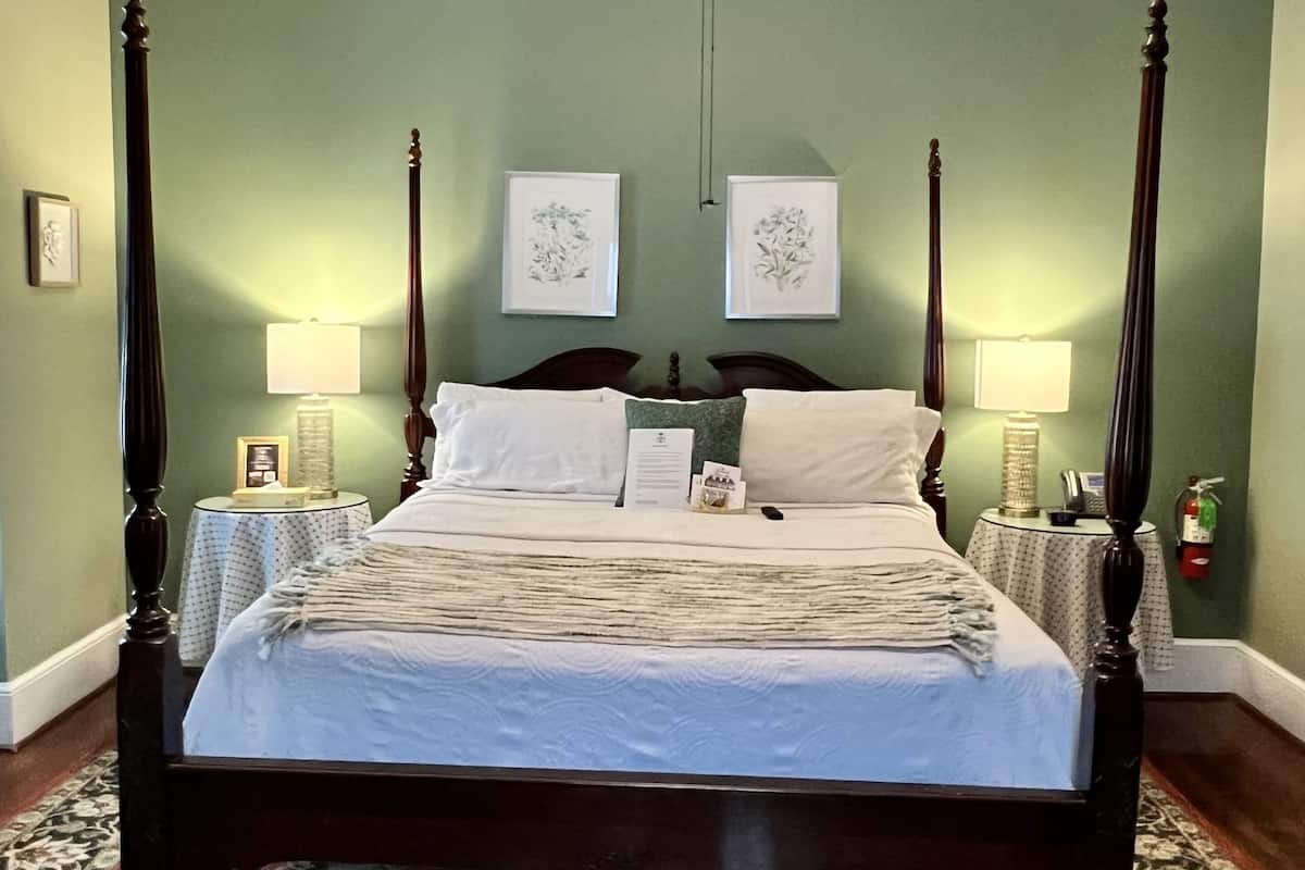 Un letto a baldacchino con finitura scura, un tappeto decorato, due lampade a parete e una ventola a soffitto.