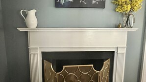 A fireplace with a white mantel, a decorative screen, and a painting of flowers above it. - Barksdale House Inn (Charleston)