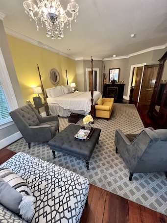 A spacious living room with a large bed, a chandelier, and a fireplace.