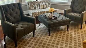 A living room with a tufted sofa, two armchairs, a patterned ottoman, and a chandelier. - Barksdale House Inn (Charleston)
