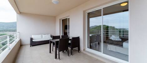 A balcony with a dining table and chairs, a sofa, and a sliding glass door leading to a bedroom.