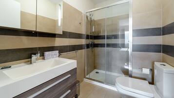 A modern bathroom with a glass-enclosed shower, a white sink, and a toilet.