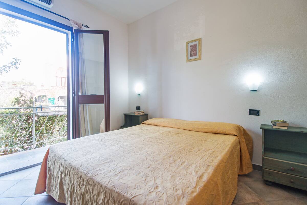 Une chambre à coucher comprenant un lit, une table de chevet, une commode, une fenêtre et une porte.