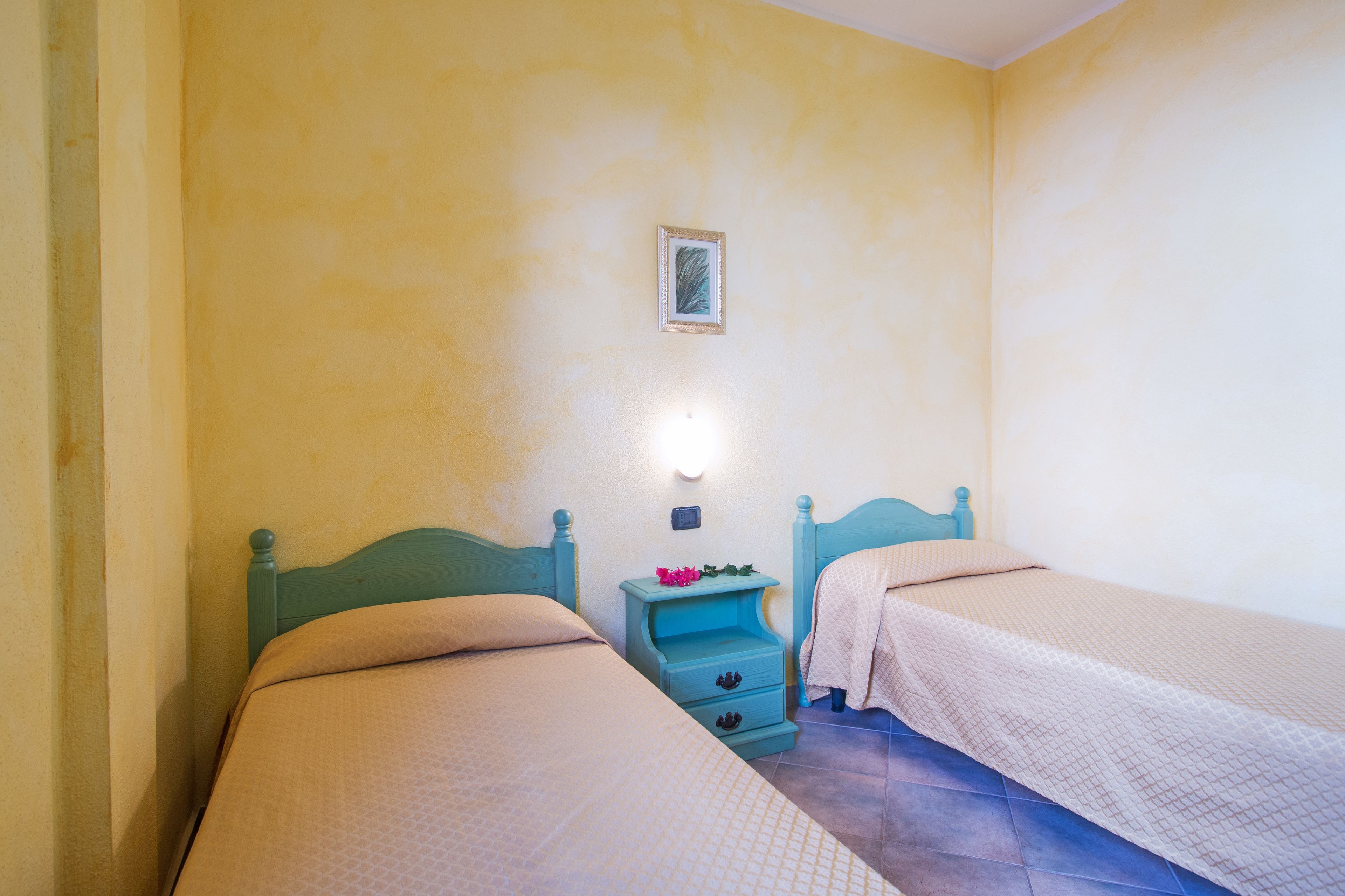 Una stanza con due letti, un comodino con una lampada e un quadro appeso al muro.