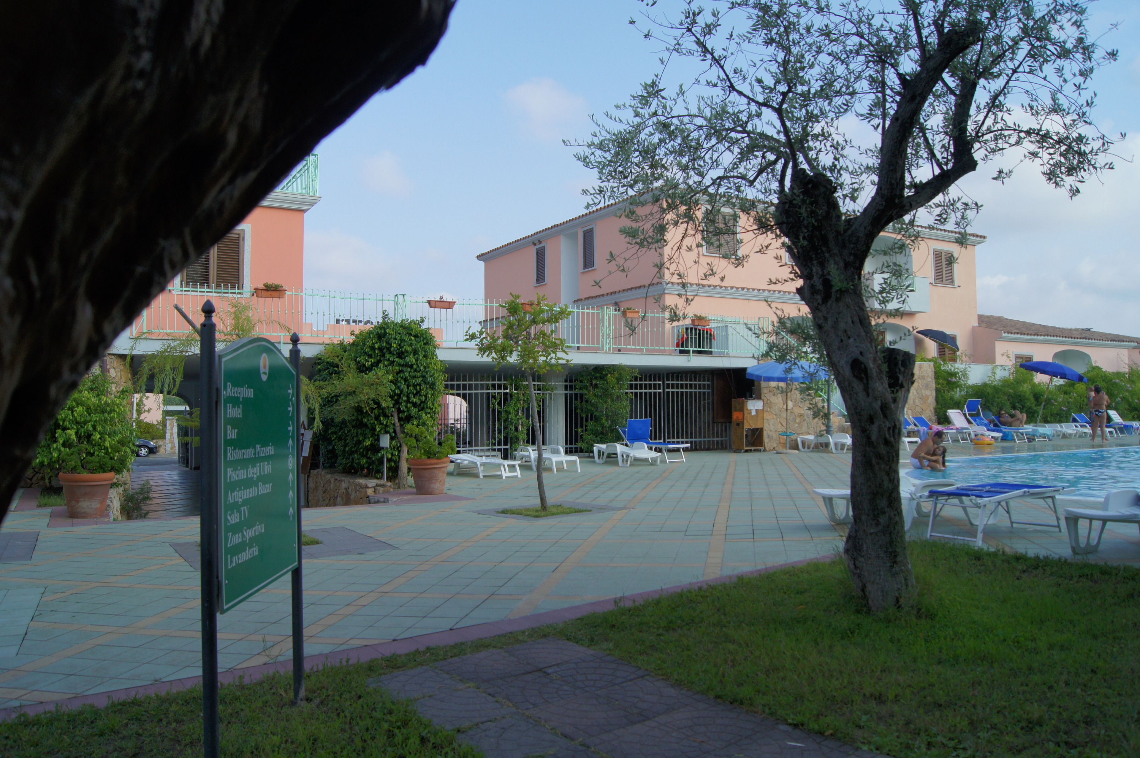 Un hotel con zona de piscina, mobiliario exterior y un cartel que enumera los servicios.