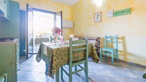 Un área de comedor con una mesa preparada para dos, una silla y vistas a un balcón a través de un umbral abierto.