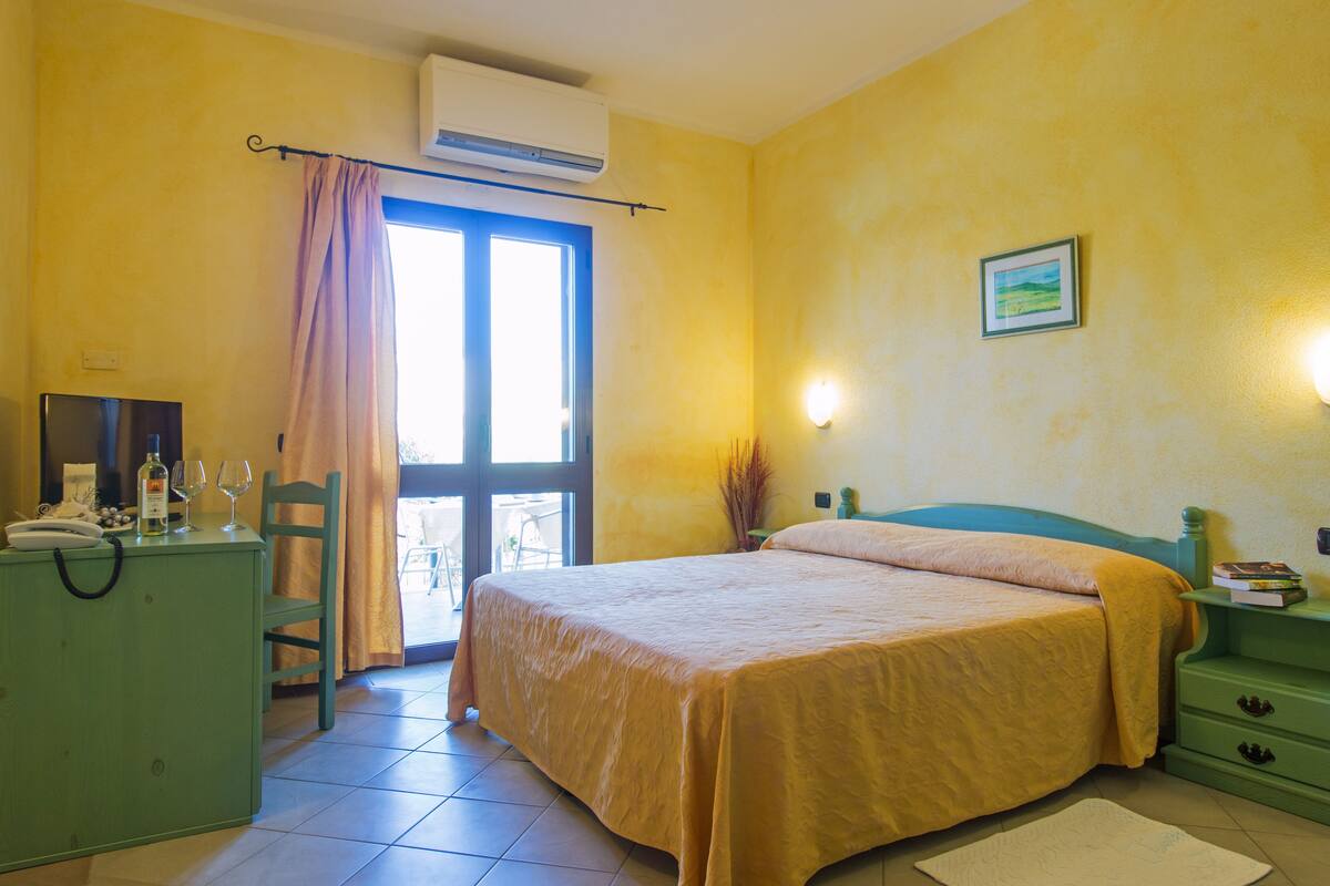 Une chambre d’hôtel comprenant un lit, un bureau avec un téléphone et des lunettes, une chaise, une table de chevet avec des livres et un tableau accroché au mur.