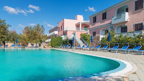 Una piscina con sillones de descanso y un edificio con balcones.