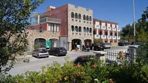 Un edificio con varios balcones, una zona de estacionamiento con automóviles y fachada de piedra.
