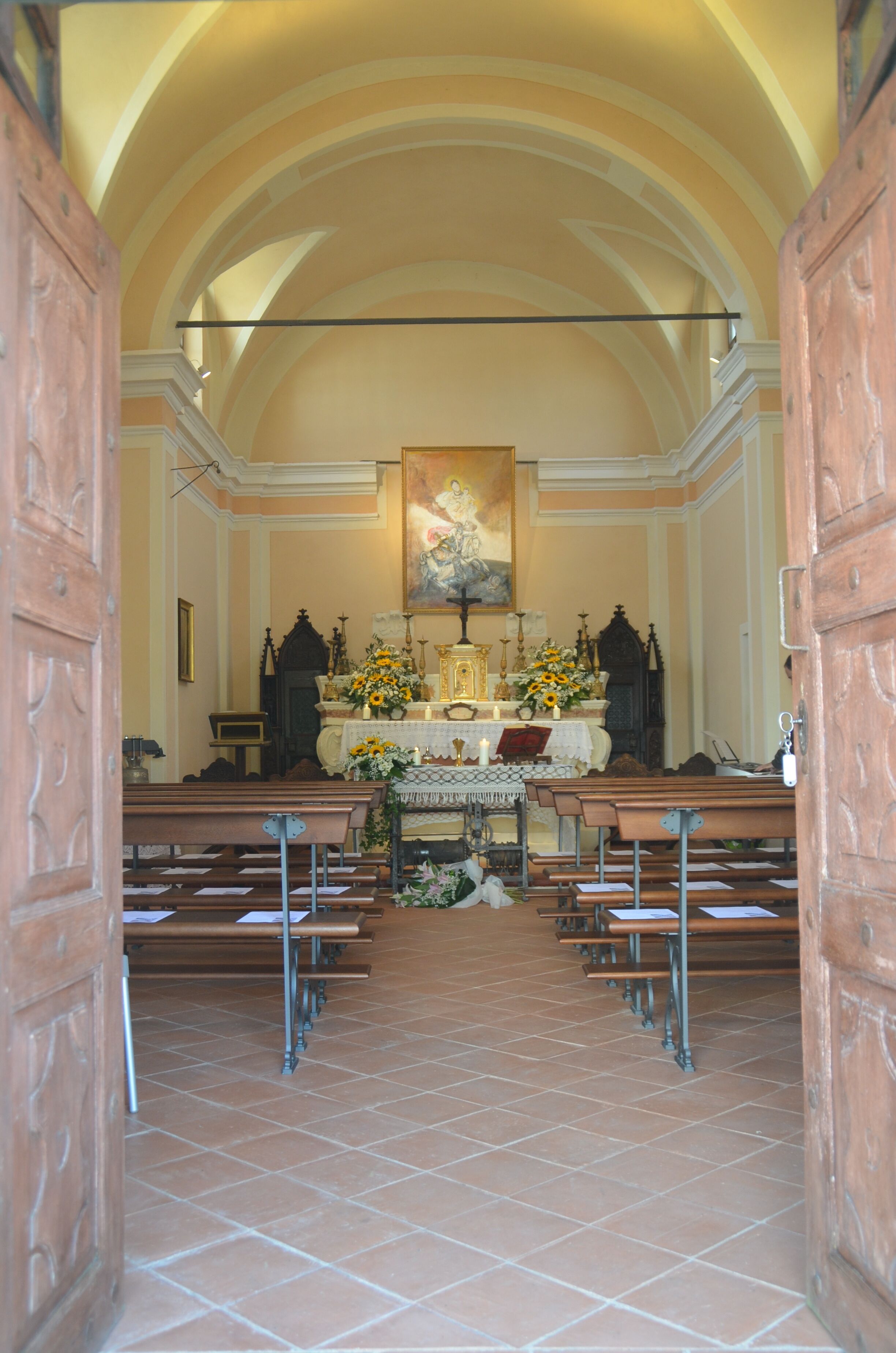 Vista del interior de una iglesia con techos abovedados, bancos y un altar central adornado con arreglos florales.