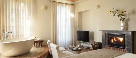Una habitación de hotel moderna con una bañera grande, un televisor de pantalla plana, una chimenea y una cama cómoda.