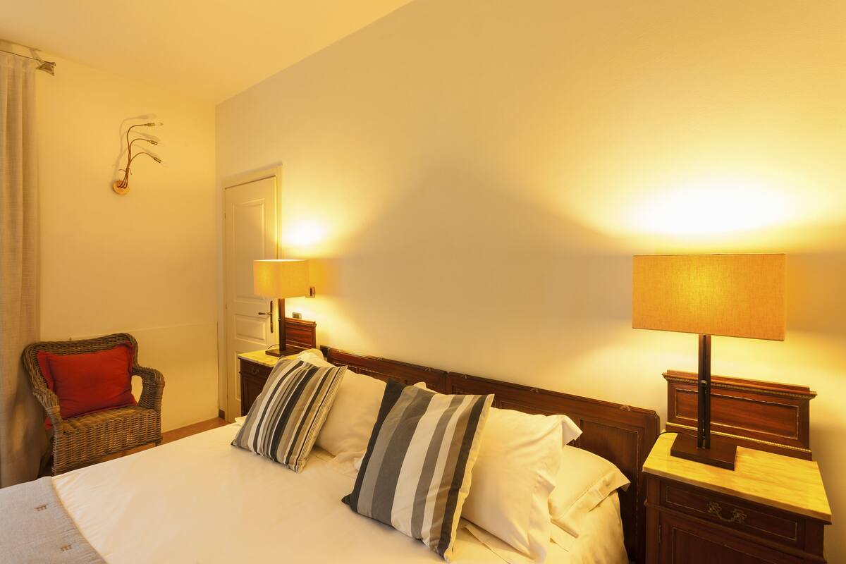 Habitación de hotel con cama, dos mesitas de noche, una silla y una lámpara de pared.