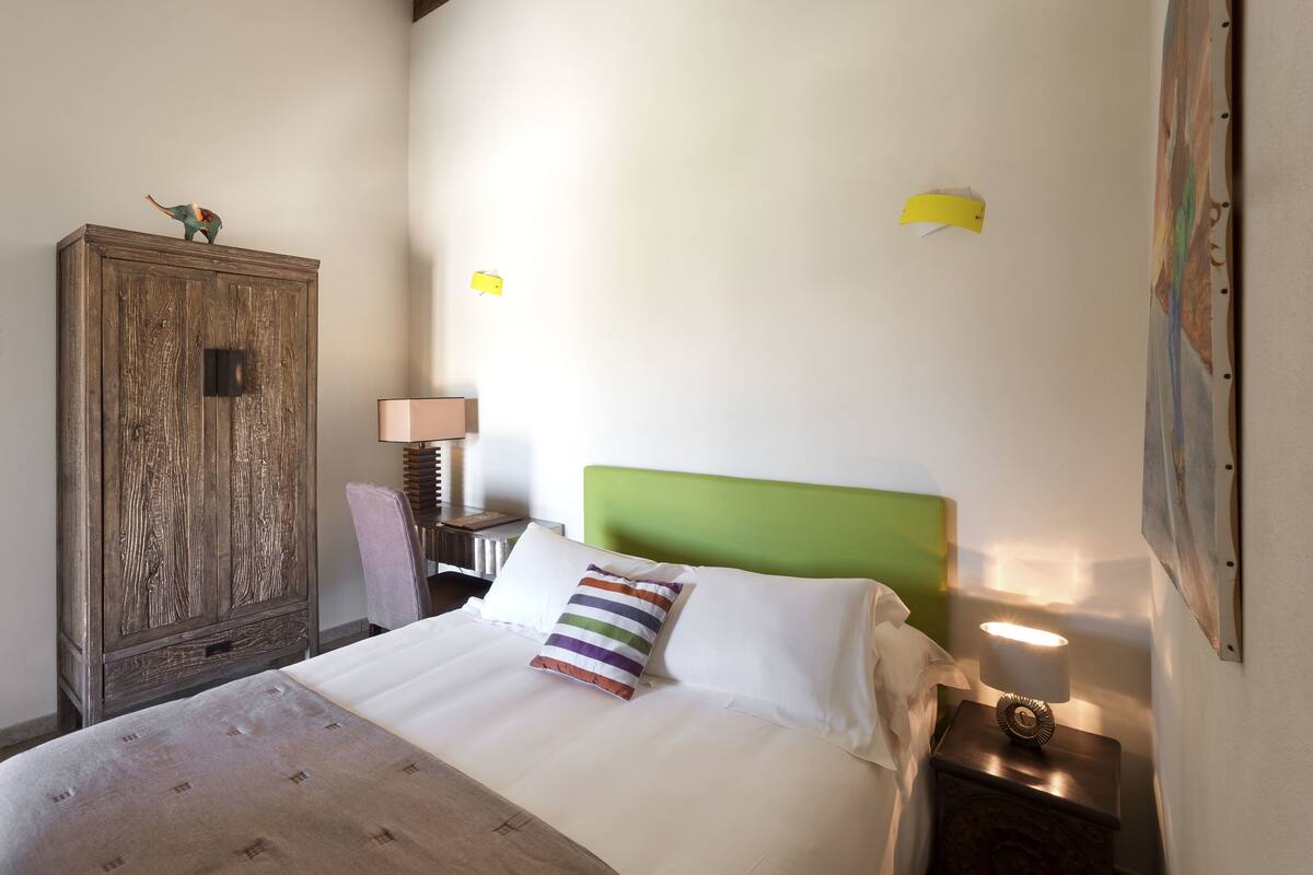 Una cama bien hecha con un cojín a rayas, cabecera verde y un armario de madera.