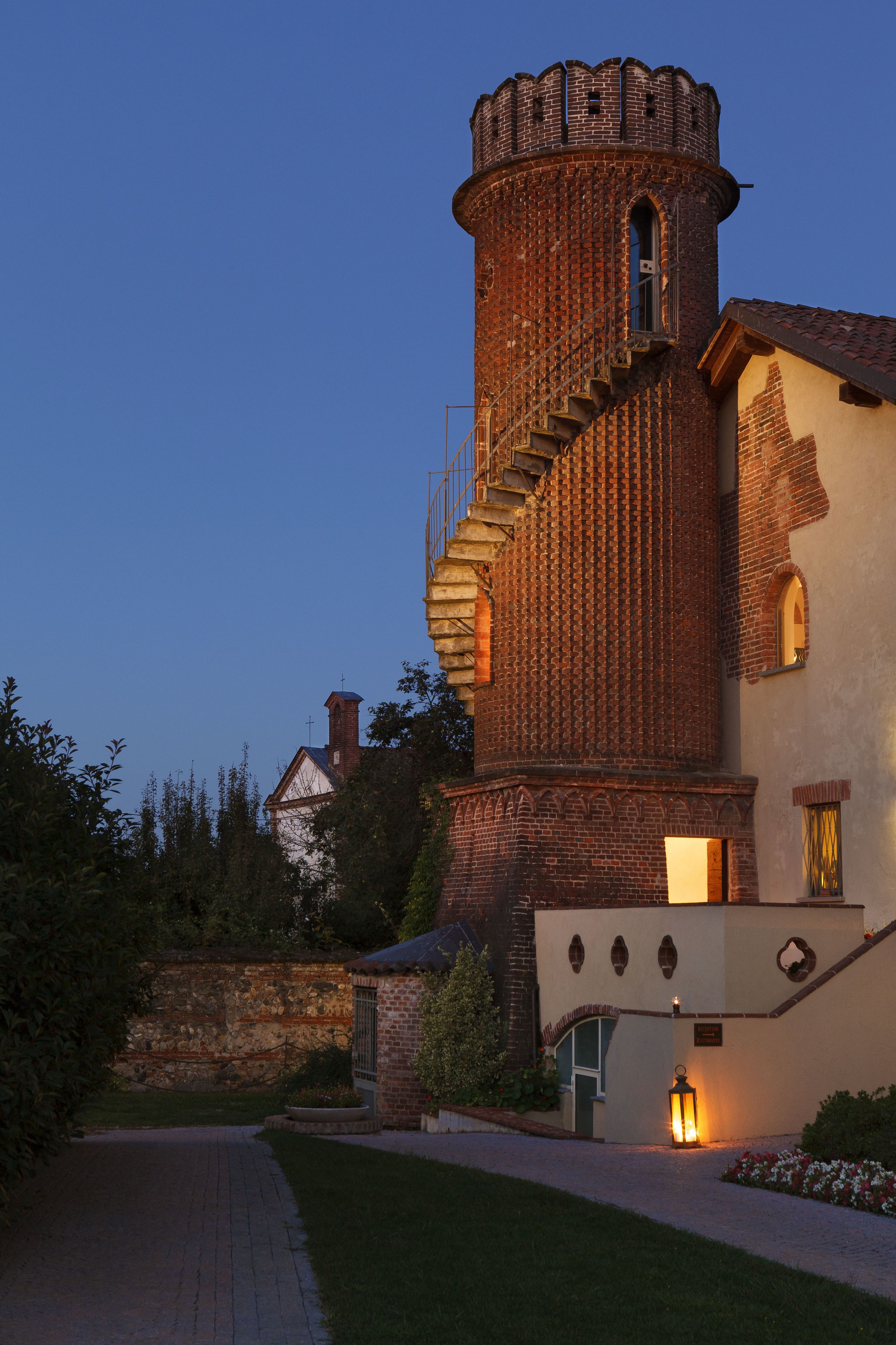 A brick tower with a spiral staircase and a lit lantern at the base.