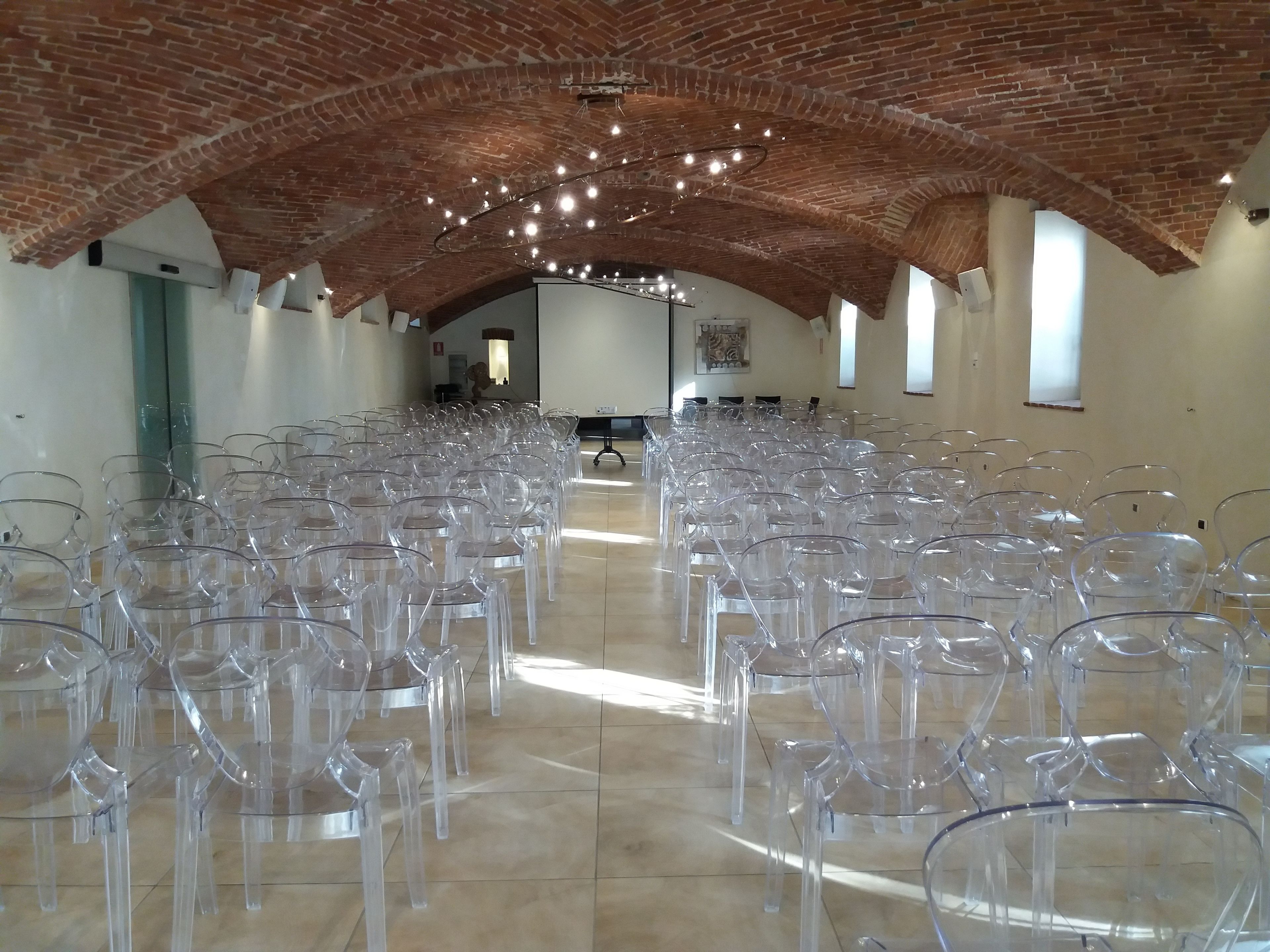 A spacious hall with rows of clear plastic chairs, a brick ceiling, and a modern light fixture.