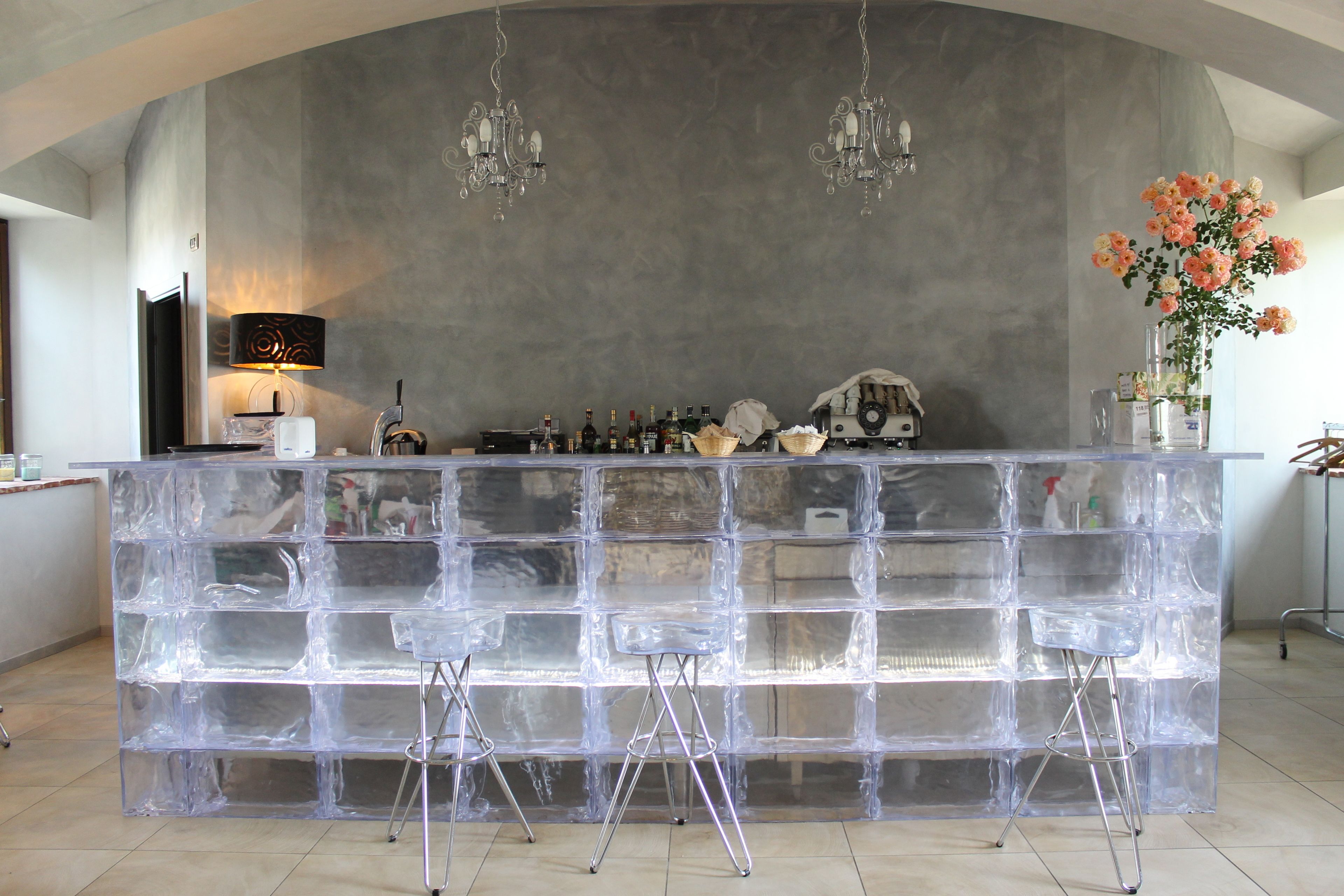 A bar area with a clear ice block counter, three bar stools, and a chandelier.
