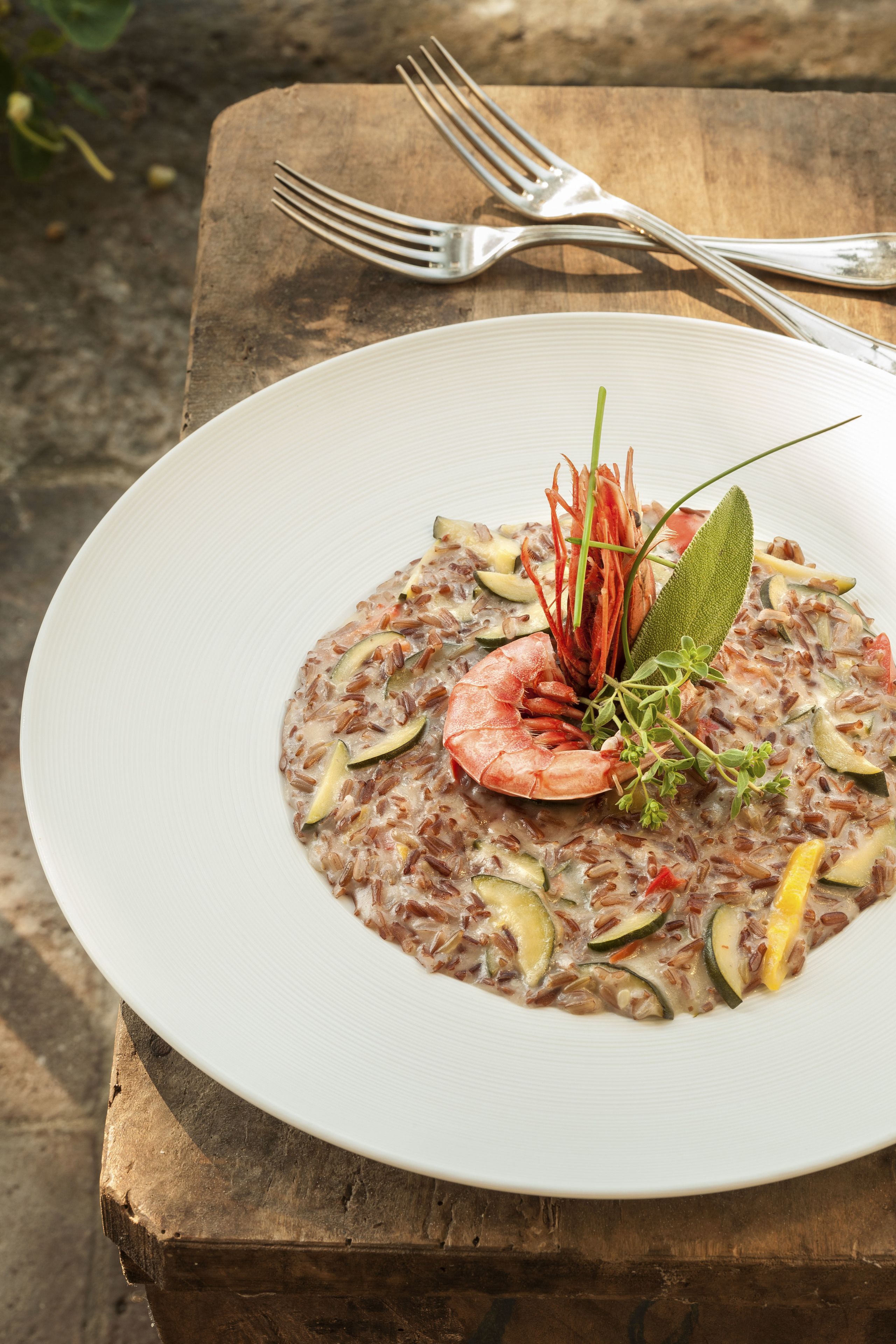 Un plato de risotto de mariscos con camarones y verduras sobre una mesa de madera.