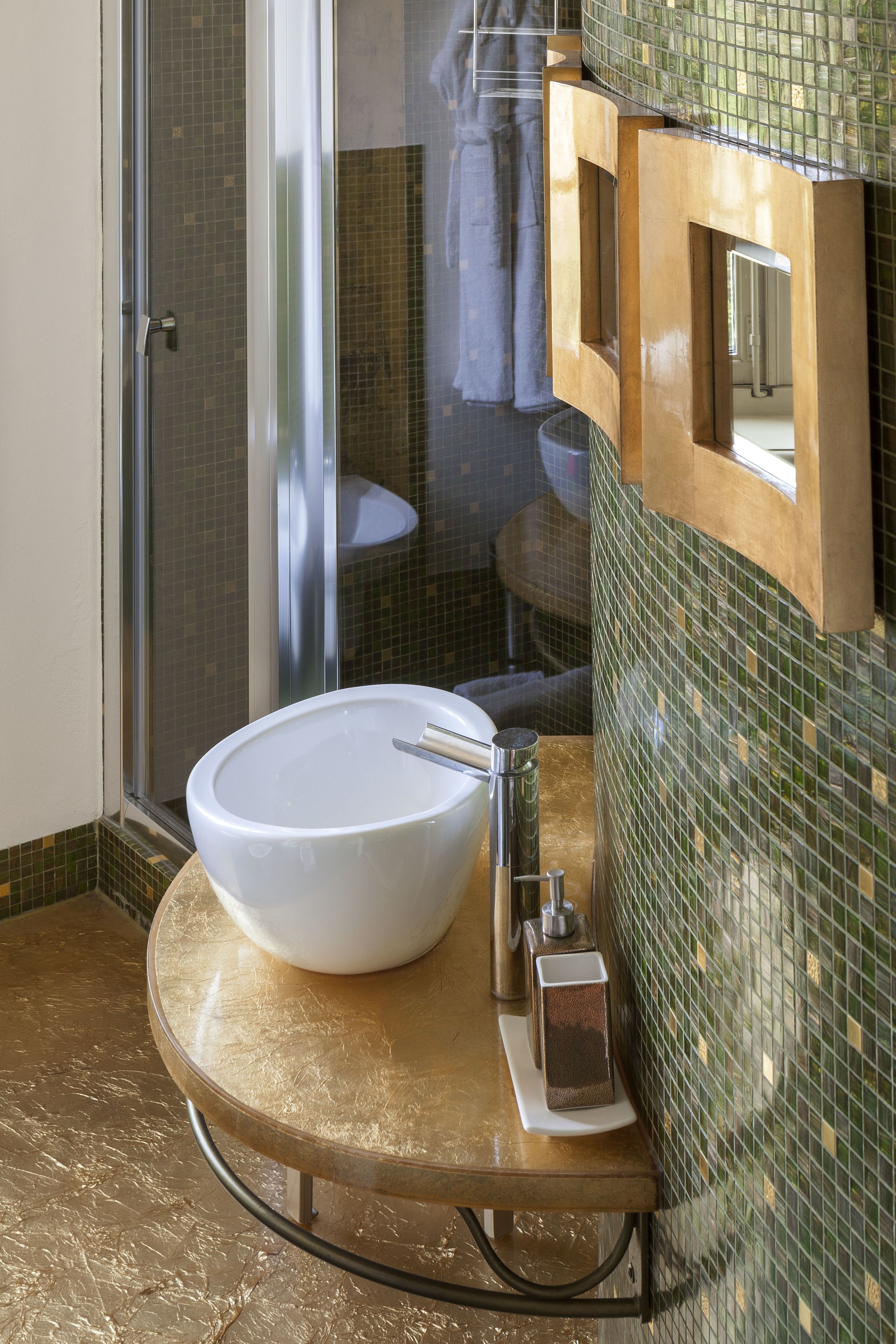 A bathroom with a large white sink, a glass shower enclosure, and a tiled wall with a wooden frame.