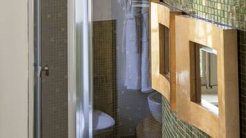 A bathroom with a large white sink, a glass shower enclosure, and a tiled wall with a wooden frame.