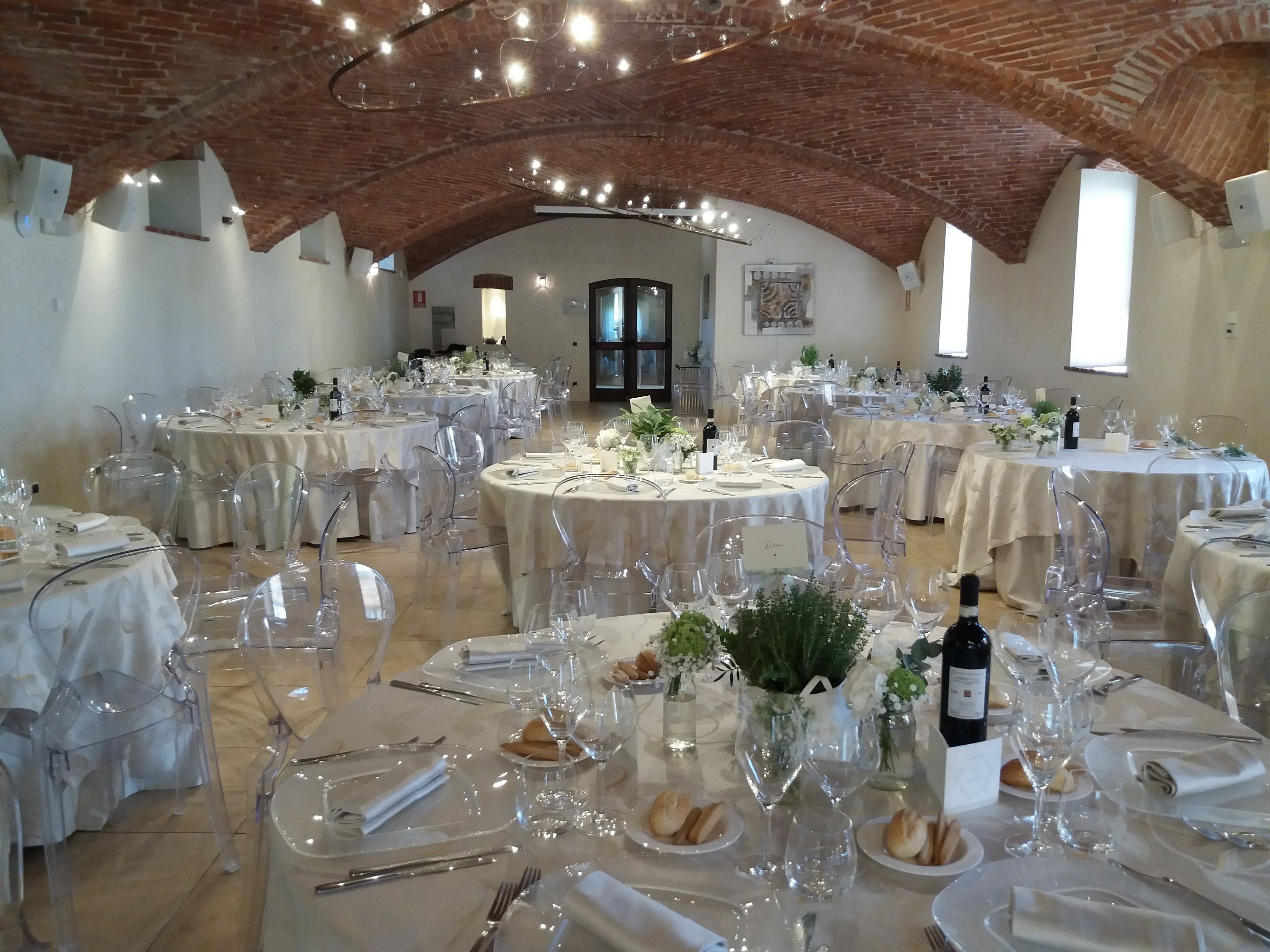 A banquet hall with round tables set for a formal event, featuring clear chairs, white tablecloths, and glassware.