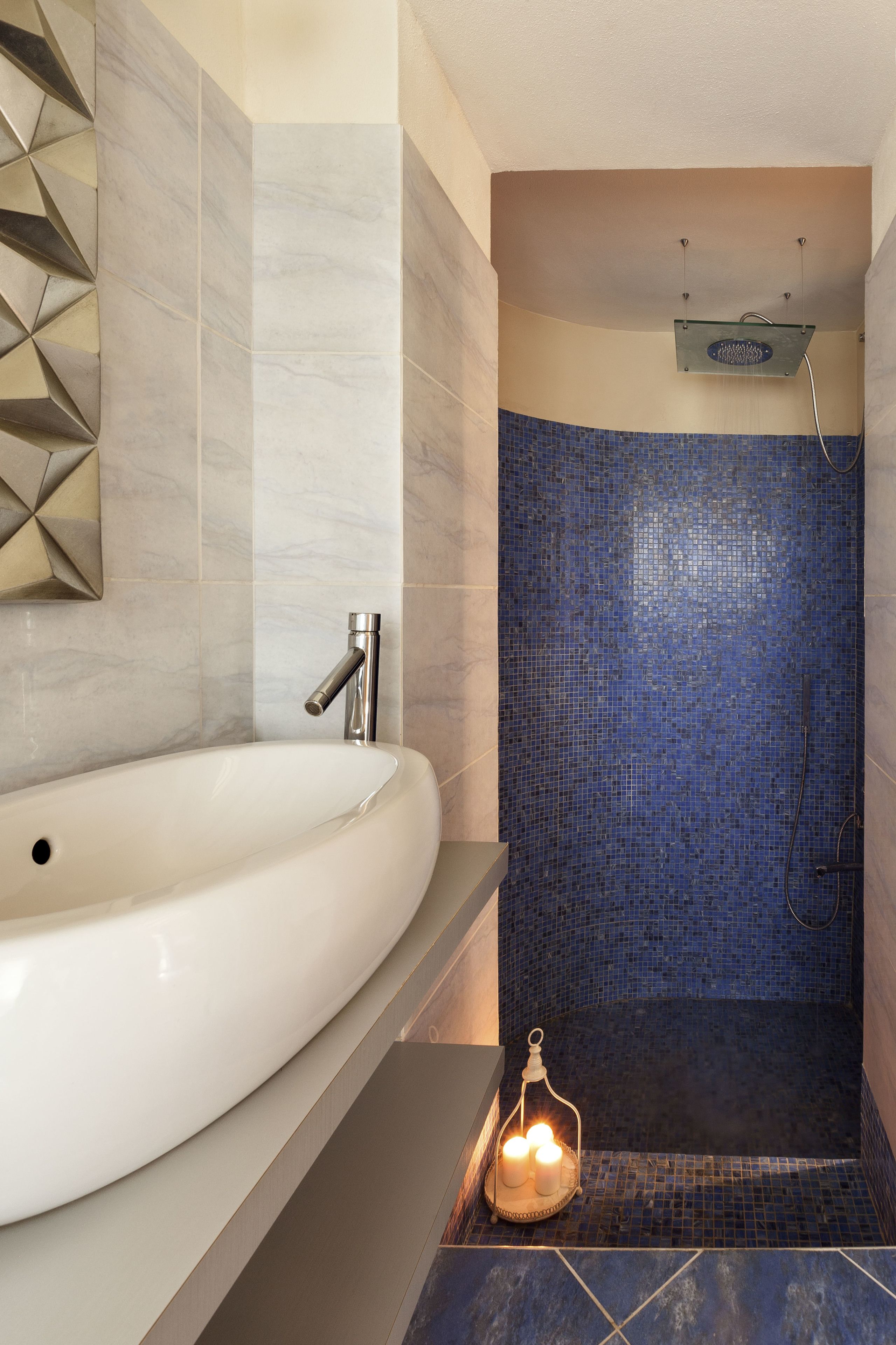 Un baño con un lavamanos blanco, una ducha con mosaicos azules y un diseño geométrico en la pared.