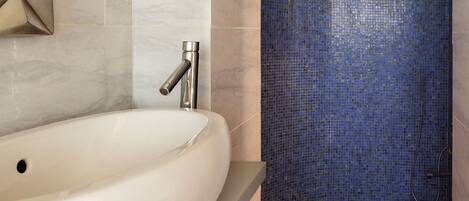 Un baño con un lavamanos blanco, una ducha con mosaicos azules y un diseño geométrico en la pared.