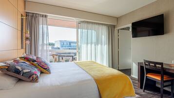 A hotel room with a bed, a desk, a chair, a TV, and a view of the outside.