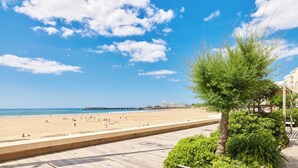 Una playa con cielo despejado, un paseo marítimo y un muelle a lo lejos.