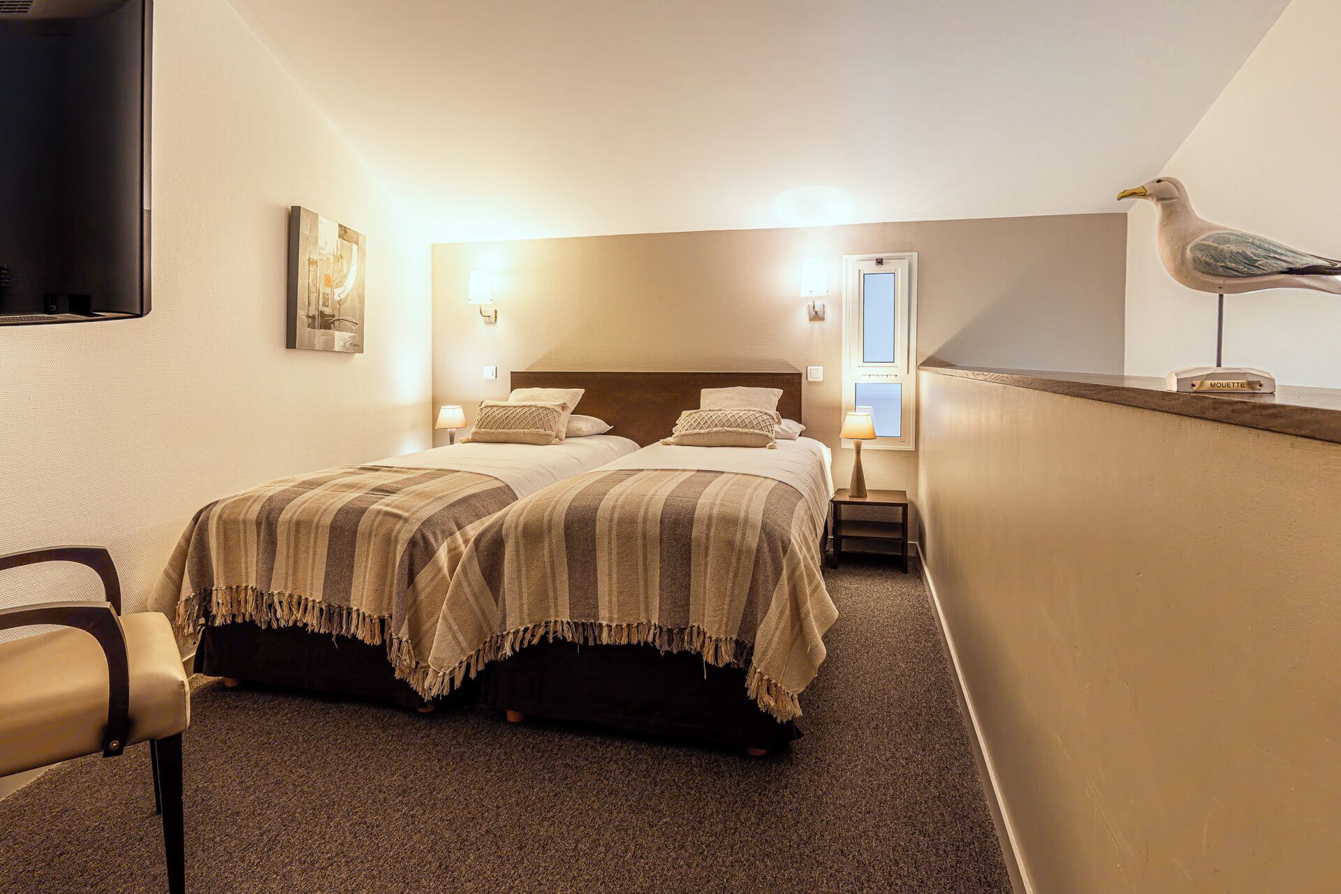 A hotel room with two beds, a chair, a seagull decoration, and a wall-mounted TV.