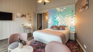 Un dormitorio con cama, dos sillas, escritorio, televisión y un mural de pared colorido.