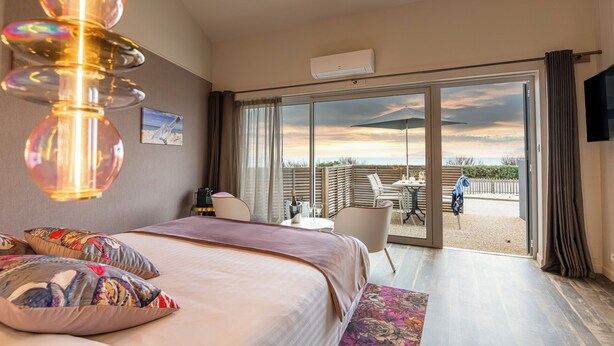 Un dormitorio con cama, escritorio y vista a la playa a través de amplios ventanales correderas.