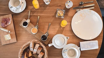 Una escena de desayuno con una mesa de madera, platos, tazas, cubiertos, pan y bebidas.