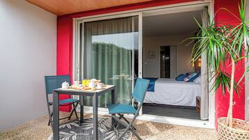 Un balcón con una mesa dispuesta para el desayuno, una silla y una cama visible a través de una puerta corrediza abierta.