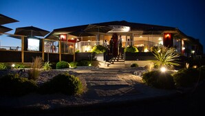 Un restaurante con terraza, entrada cubierta y un camino bien iluminado.