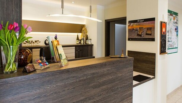 A reception area with a wooden reception desk, a vase of tulips, a framed picture, and a map on the wall. - Hotel Weiße Elster (Zeitz)