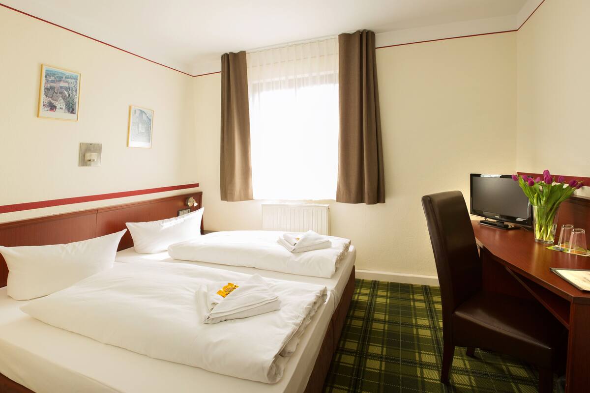 A hotel room with two beds, a desk with a television, and a chair.