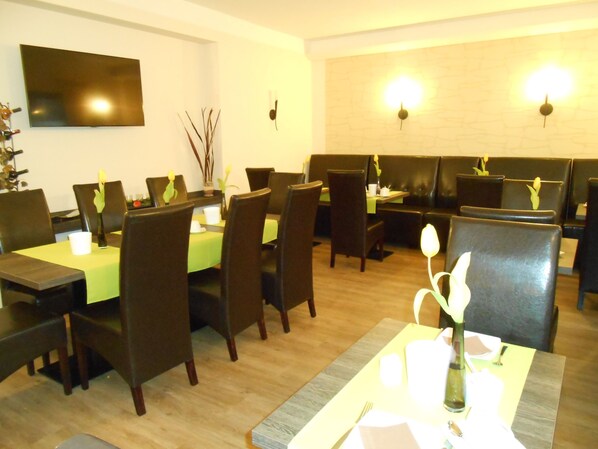A restaurant with multiple tables and chairs, a flat-screen TV mounted on the wall, and wall-mounted lighting fixtures. - Hotel Weiße Elster (Zeitz)