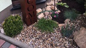 A wooden welcome sign with a hanging planter above it, surrounded by a gravel pathway and various plants. - Hotel Weiße Elster (Zeitz)