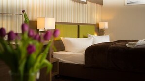 A hotel room with a bed, two bedside lamps, a green headboard, and a vase with flowers. - Hotel Weiße Elster (Zeitz)