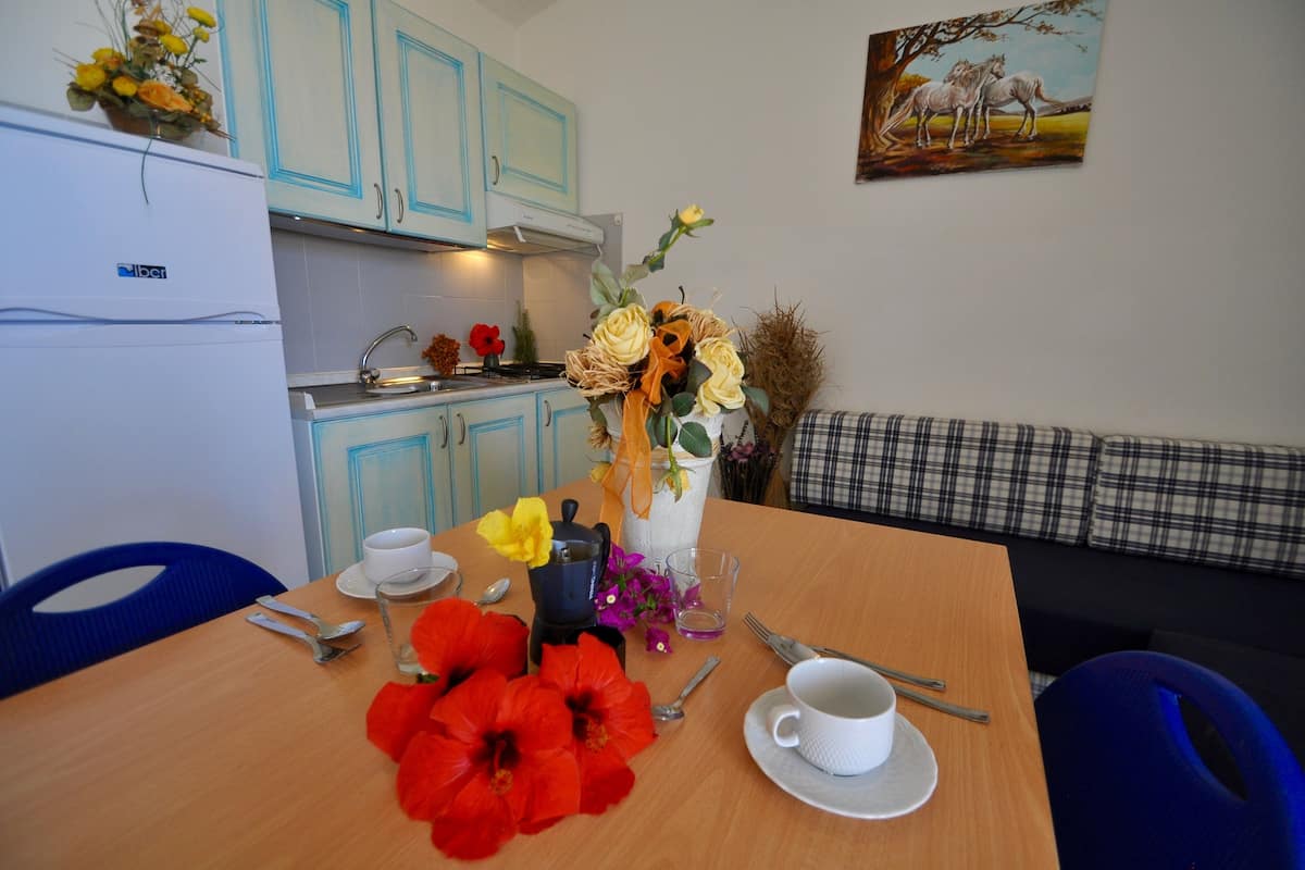 A dining area with a table set for two, a coffee maker, and a vase with flowers.