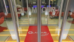Entrada de hotel con alfombra roja y las palabras "GLAMOUR Hotel" en las puertas de vidrio.