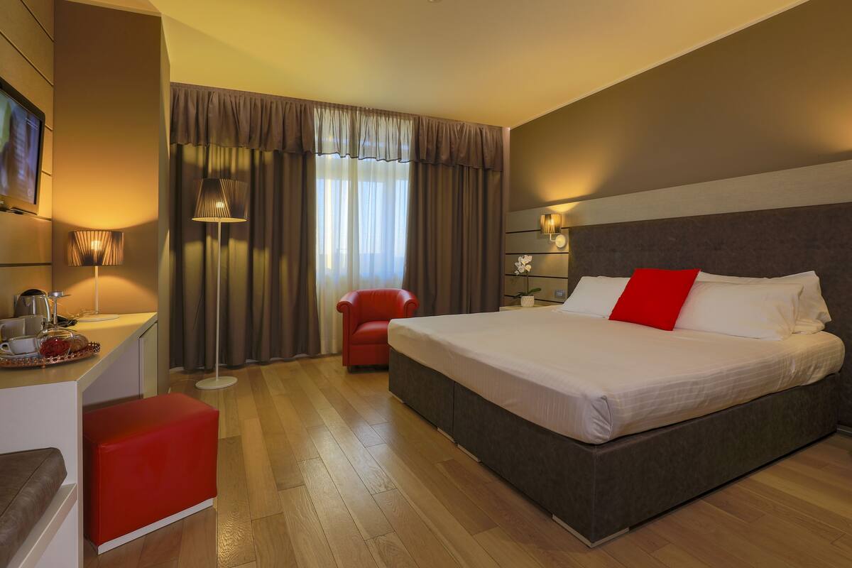 Una habitación de hotel con una cama grande, un escritorio con lámpara, una silla roja y un televisor.