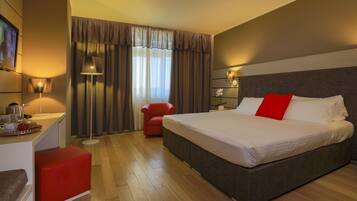 Una habitación de hotel con una cama grande, un escritorio con lámpara, una silla roja y un televisor.